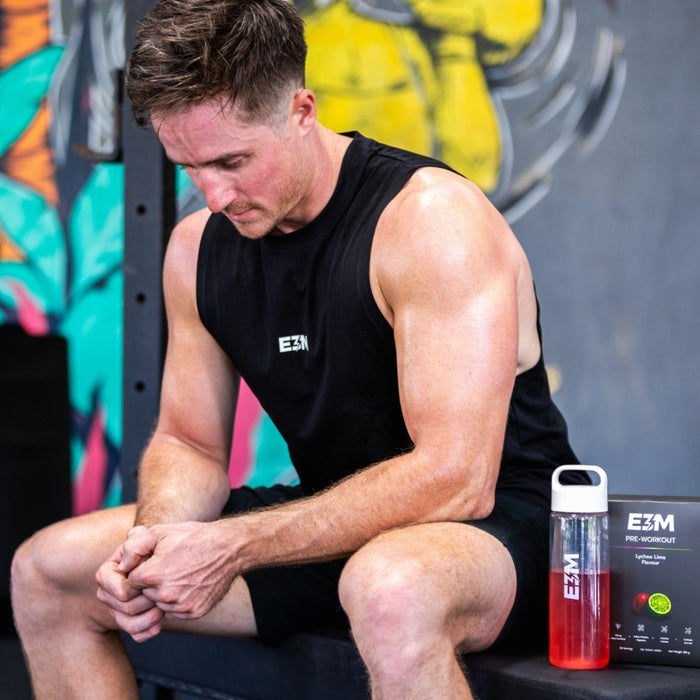 Man in the E3M Training Vest resting in the gym next to an E3M Pre Workout box and drink bottle