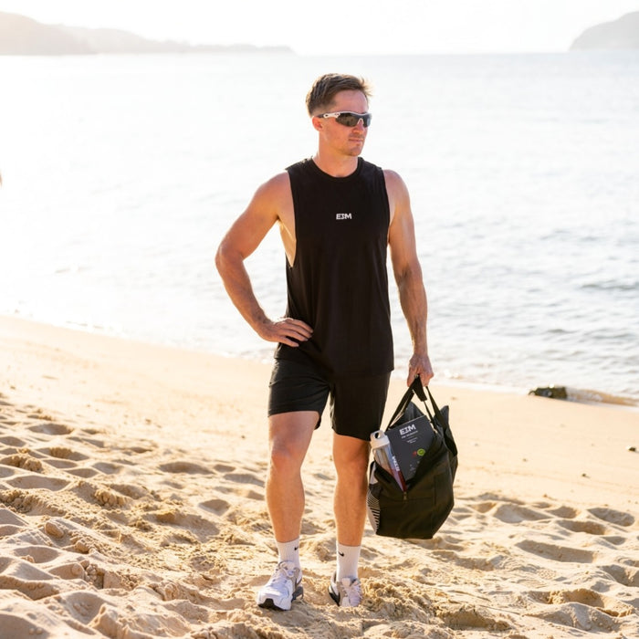 Man wearing the black E3M Training Vest on a beach carrying a gym bag